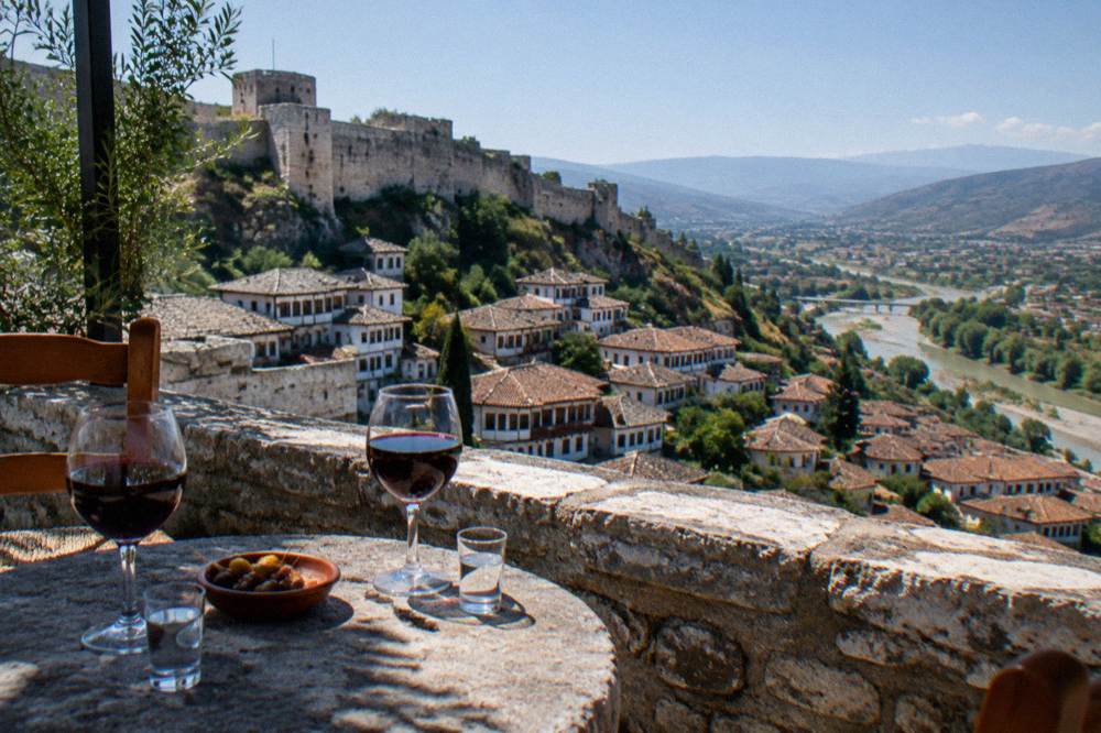Glasses of red wine and small raki glasses on a stone terrace above the Ottoman rooftops of Berat