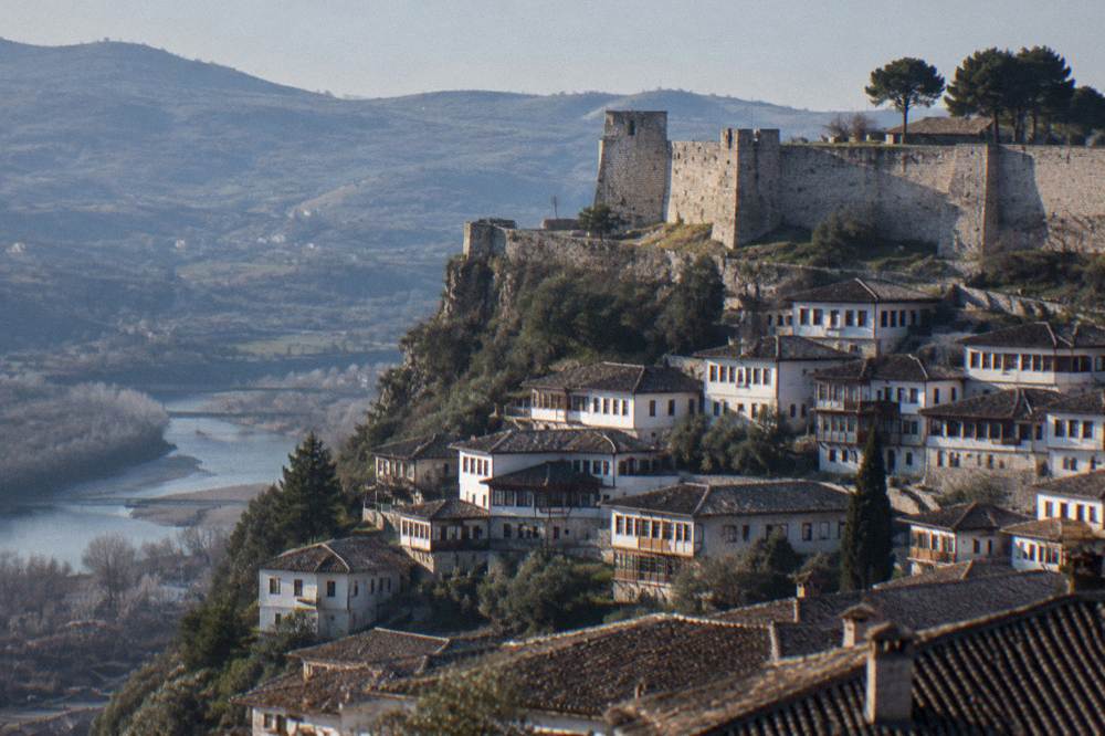 Whitewashed Ottoman houses stacked on a hillside below the stone walls of Berat Castle