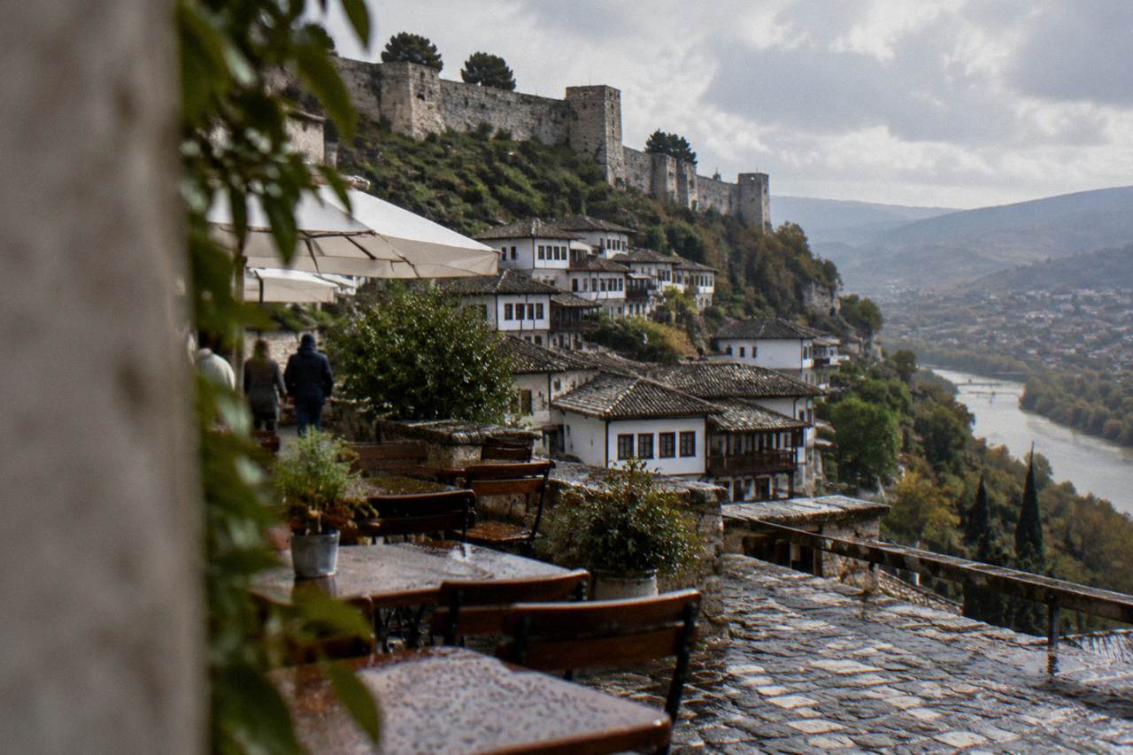 Outdoor restaurant tables on a cobbled Berat street with white Ottoman houses rising behind