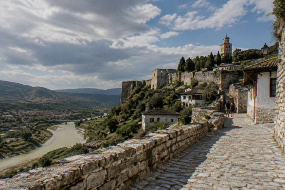 A stone street inside the old castle quarter of Berat with a church tower in the distance