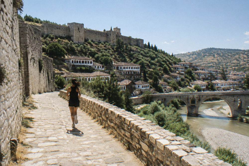 Stone bridge over the Osum River with white Ottoman houses rising on the hillside behind it