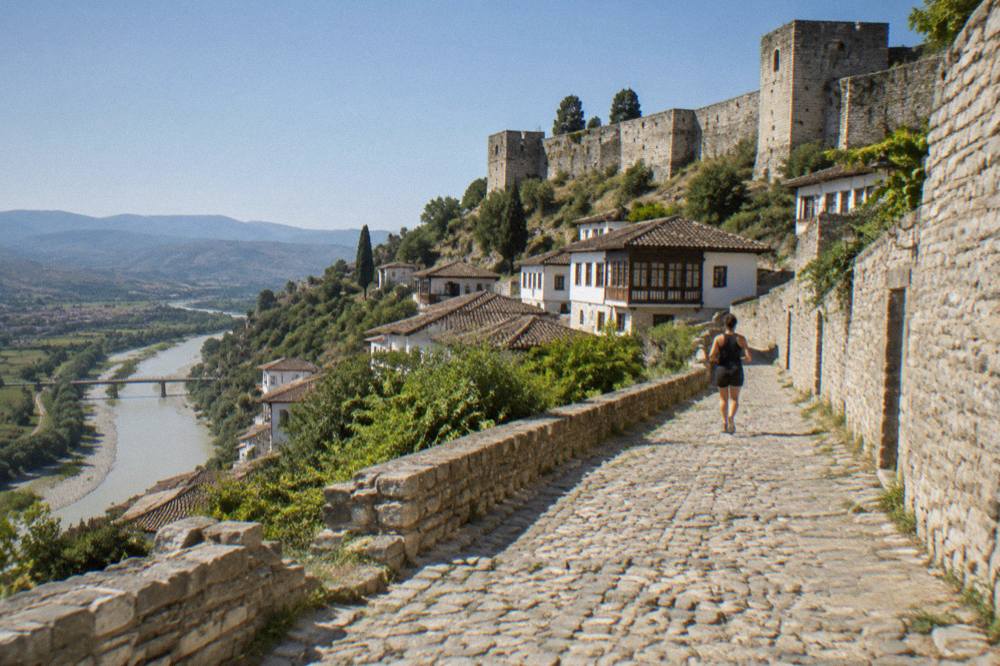 Cobbled lane climbing toward the stone walls and towers of Berat Castle above the old town