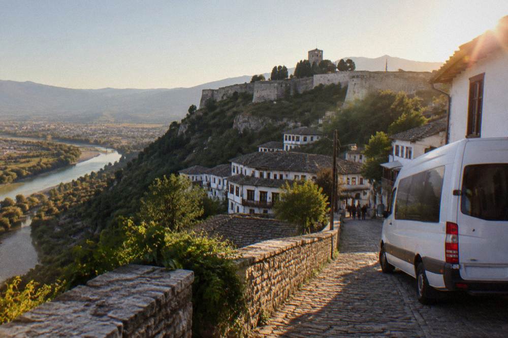 A minibus parked on a street in an old Albanian town with whitewashed hillside houses