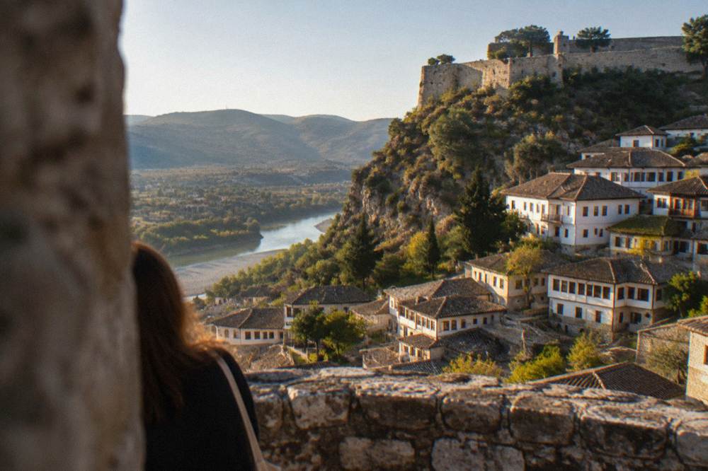 White Ottoman houses stacked on a hillside above the Osum River with the castle ridge behind
