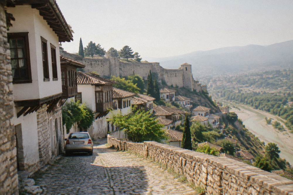 A narrow stone street of Ottoman-era houses in Berat with a car parked at the edge of the lane