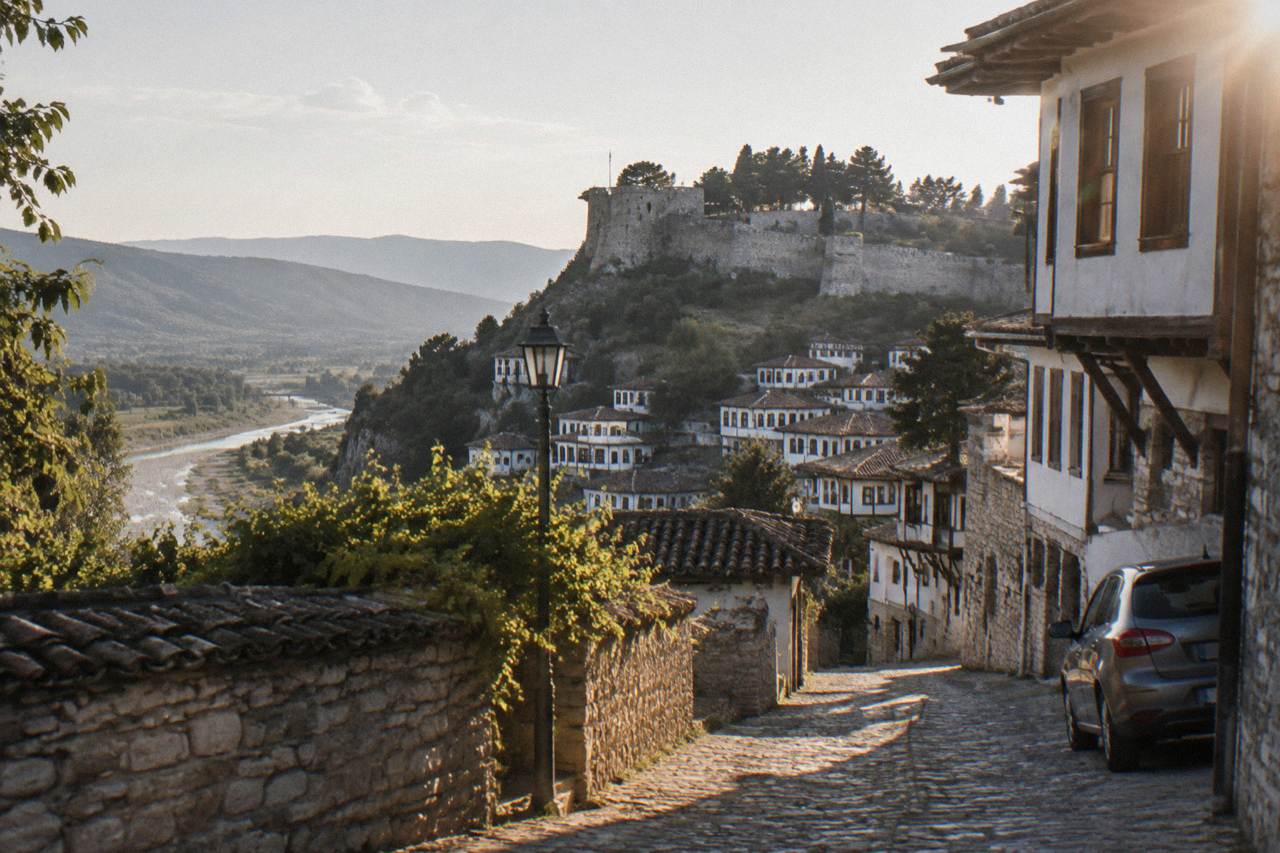 A narrow stone street of Ottoman-era houses in Berat with a car parked at the edge of the lane