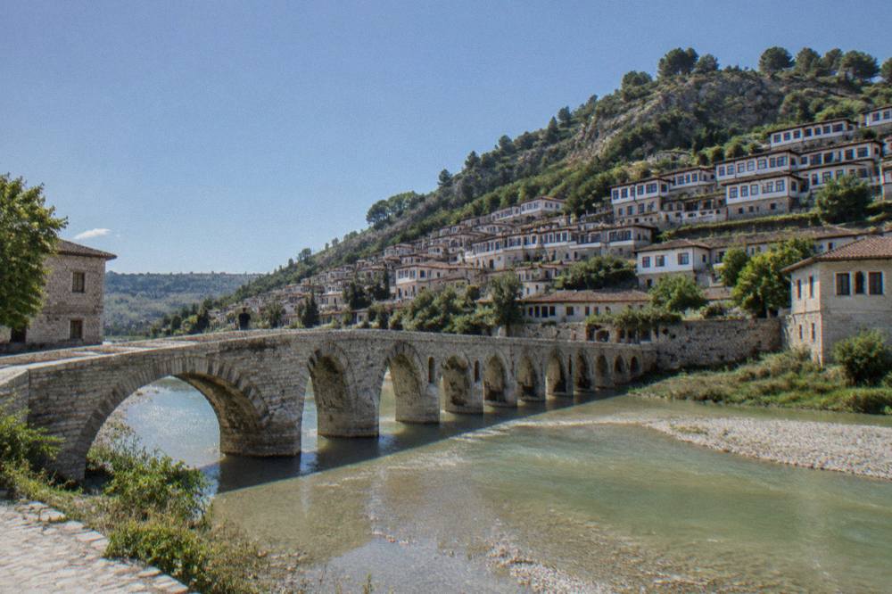 The green Osum river flowing beneath the old Gorica bridge in Berat with stone buildings on both banks