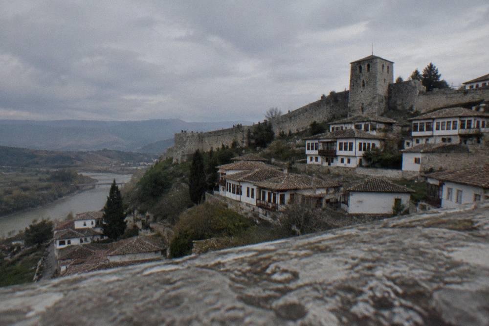 Stone walls and a defensive tower of Berat Castle above the white rooftops of the old town