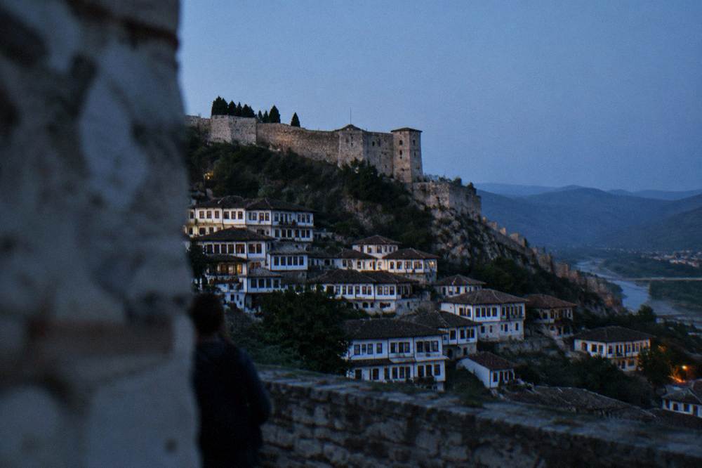White Ottoman houses stacked on a hillside above a river in Berat under a clear morning sky