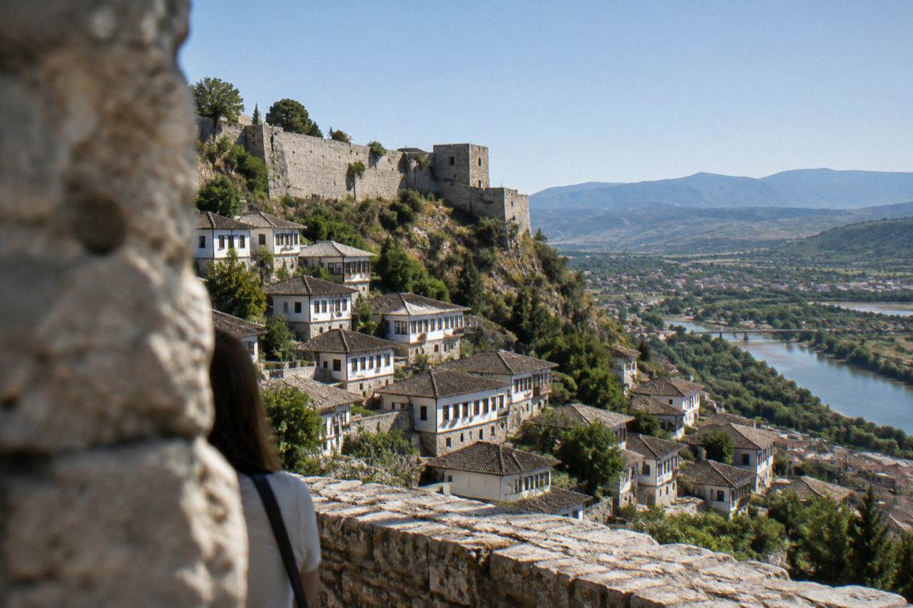 White Ottoman houses stacked on a hillside above a river in Berat under a clear morning sky