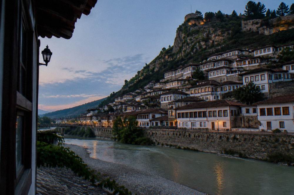 Rows of white Ottoman houses with wooden windows climbing a hillside above a river