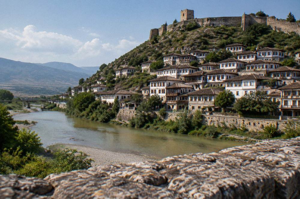 White Ottoman houses stacked on a hillside above a calm river in Berat, Albania