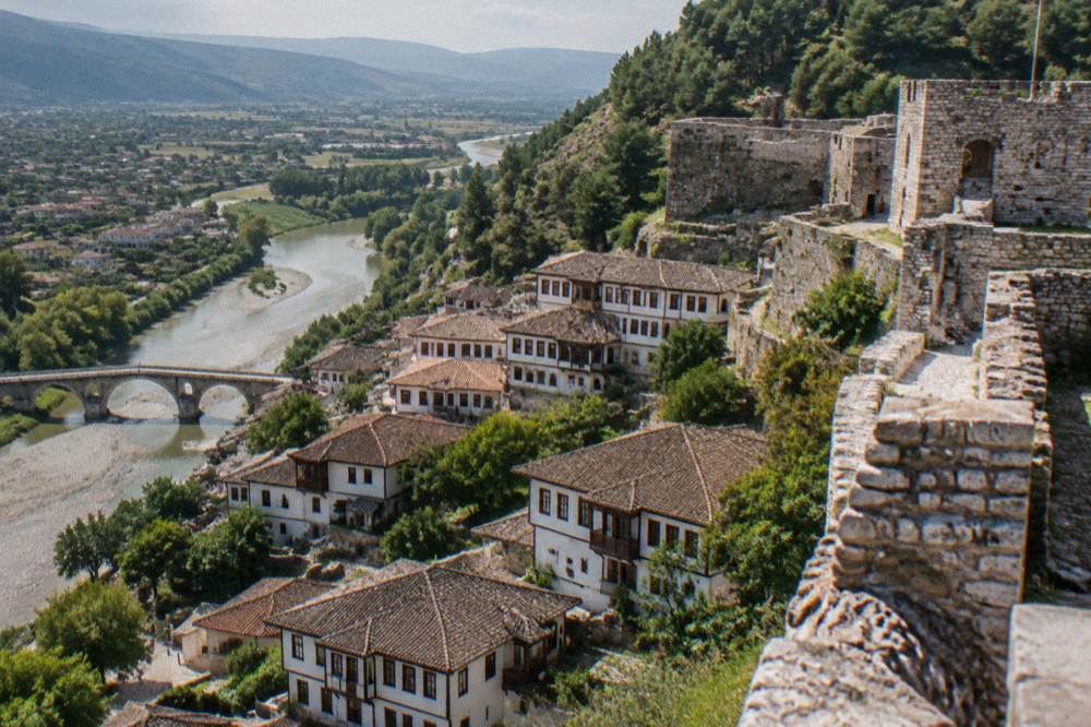 White-walled Ottoman houses stacked on a green hillside above a stone bridge