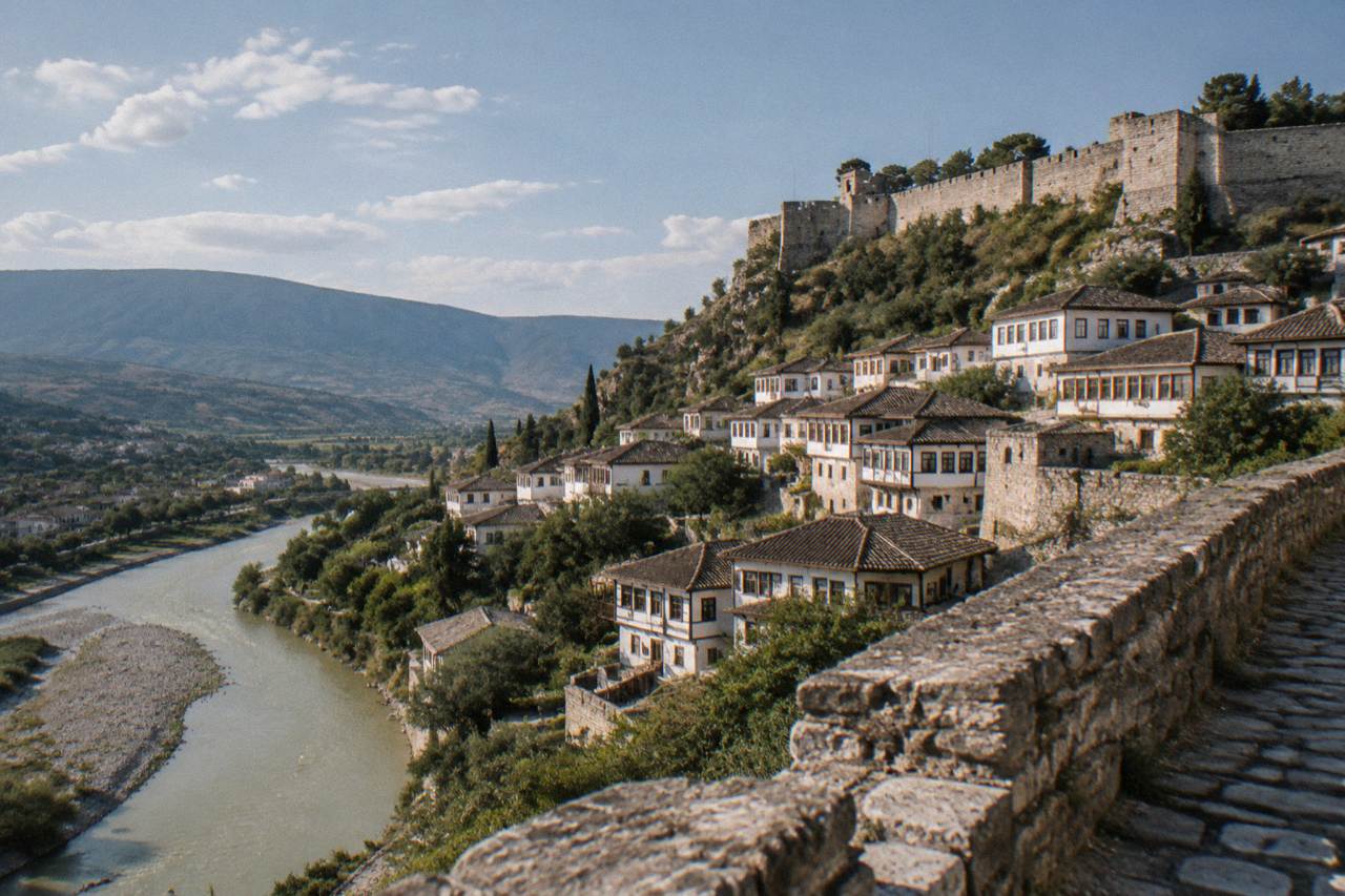 Sunlit stone houses with white walls and rows of windows rising above a river in an old Balkan town