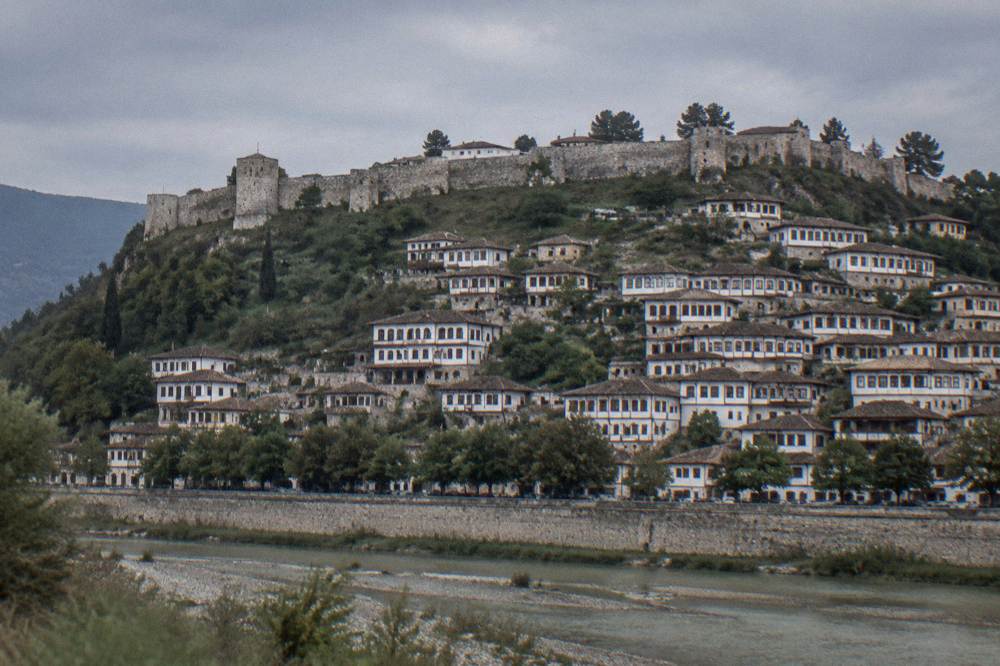 White Ottoman houses stacked on a hillside above a river in Berat