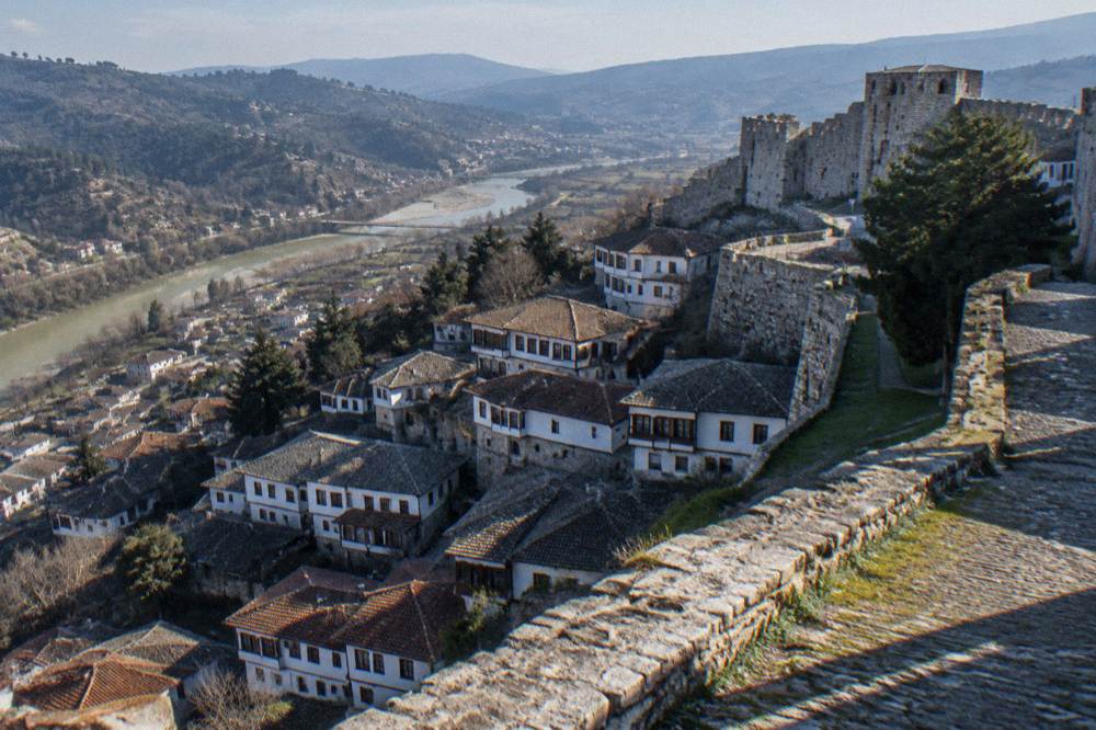 White Ottoman houses stacked on a hillside below a stone castle in Berat, Albania