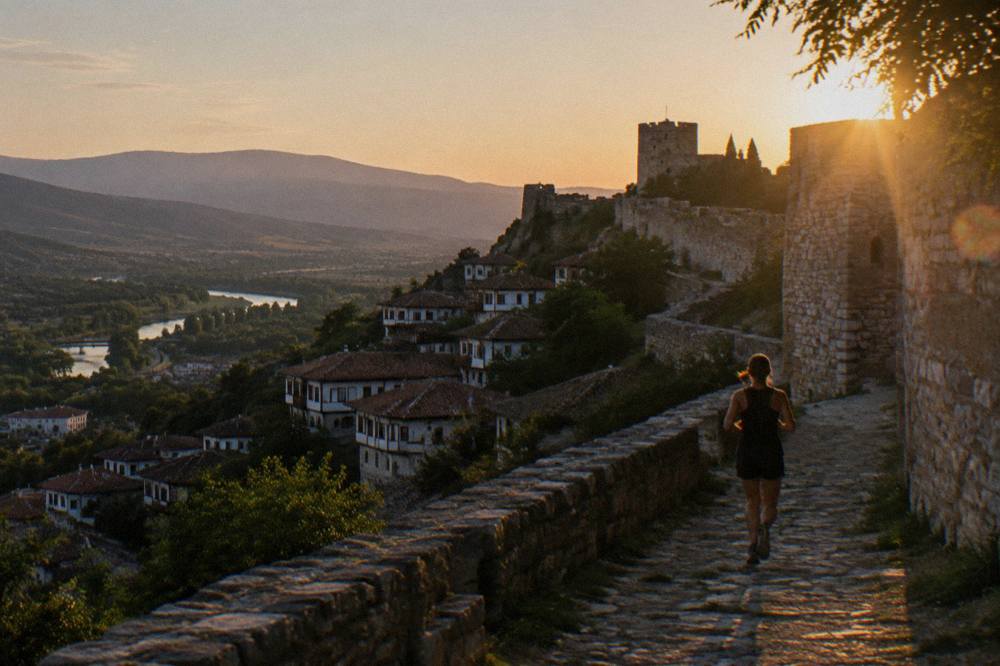 Stone walls and towers of Berat Castle above red-tiled rooftops at dusk
