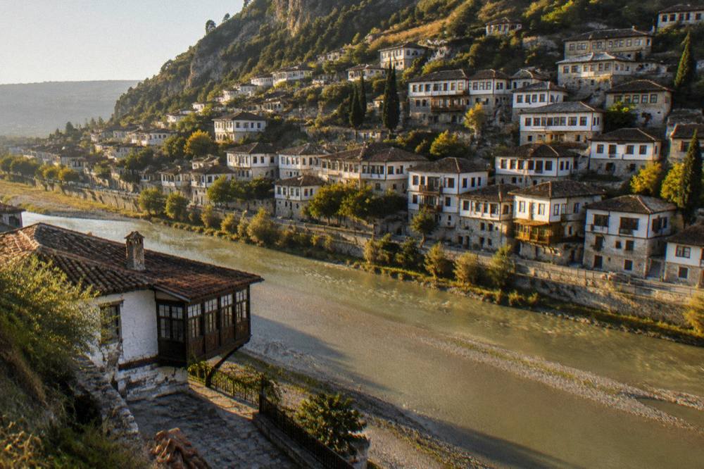 Old stone houses on a hillside seen across a river at golden hour