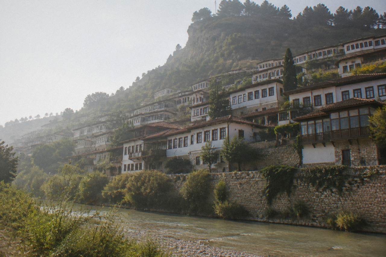 Rows of red-roofed Ottoman houses stacked on a green hillside above a river
