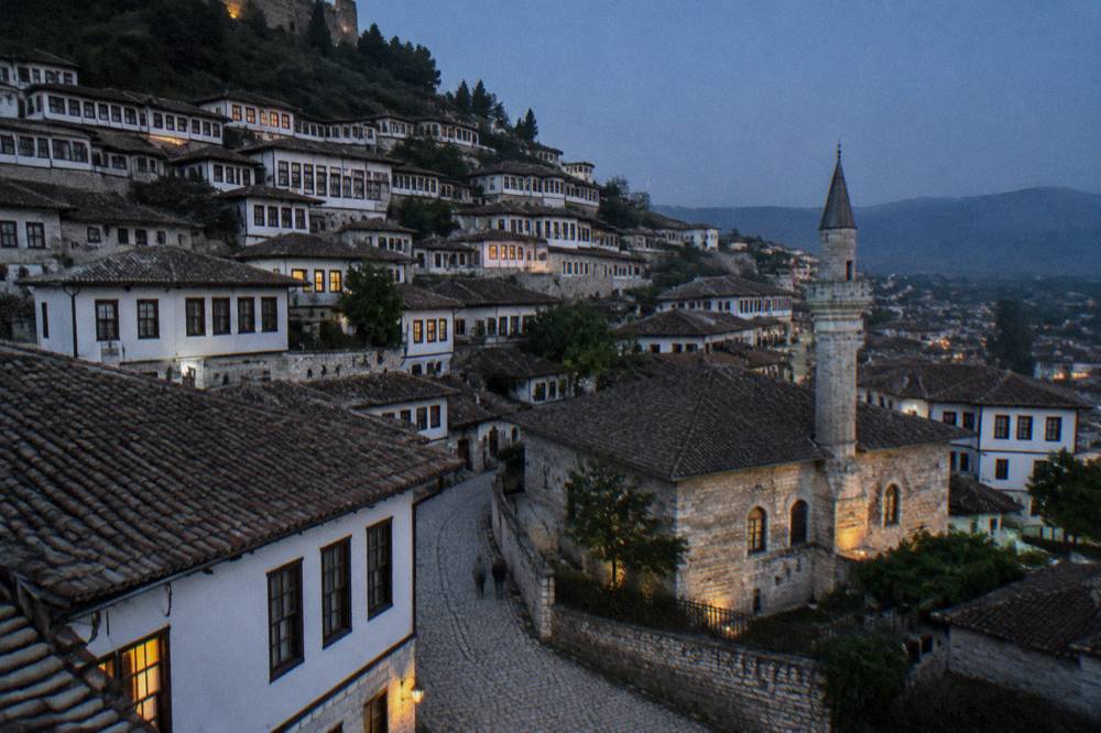 A small Ottoman stone mosque with a tiled roof beside a quiet street