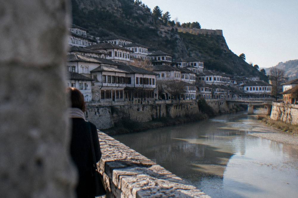 A river flowing between two hillside quarters of white houses, seen from a stone bridge