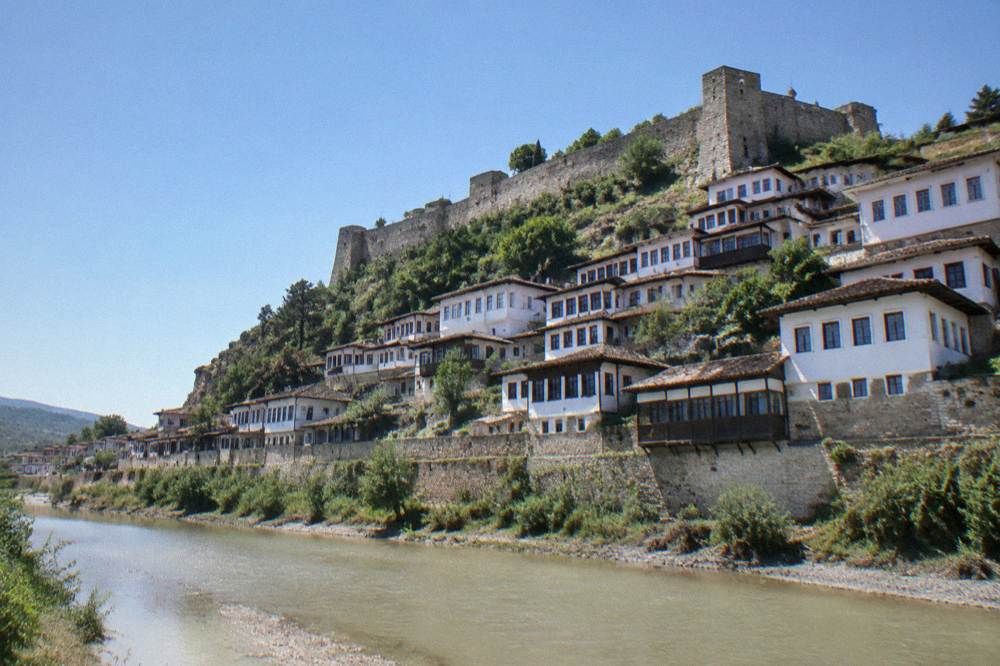 White Ottoman houses with rows of windows stacked on a hillside above a river in Berat