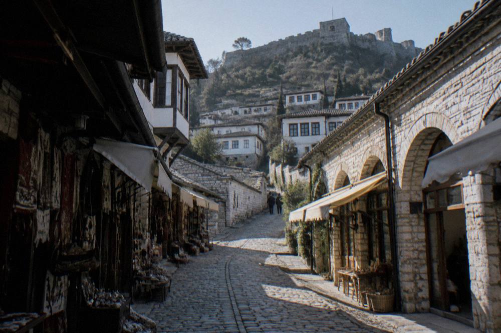 Stone lane winding uphill between white houses toward the castle walls of Berat