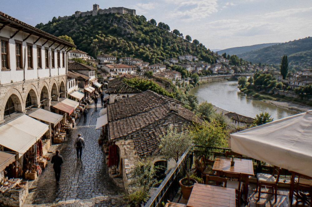Guesthouse terrace with wooden tables overlooking a river and old town rooftops