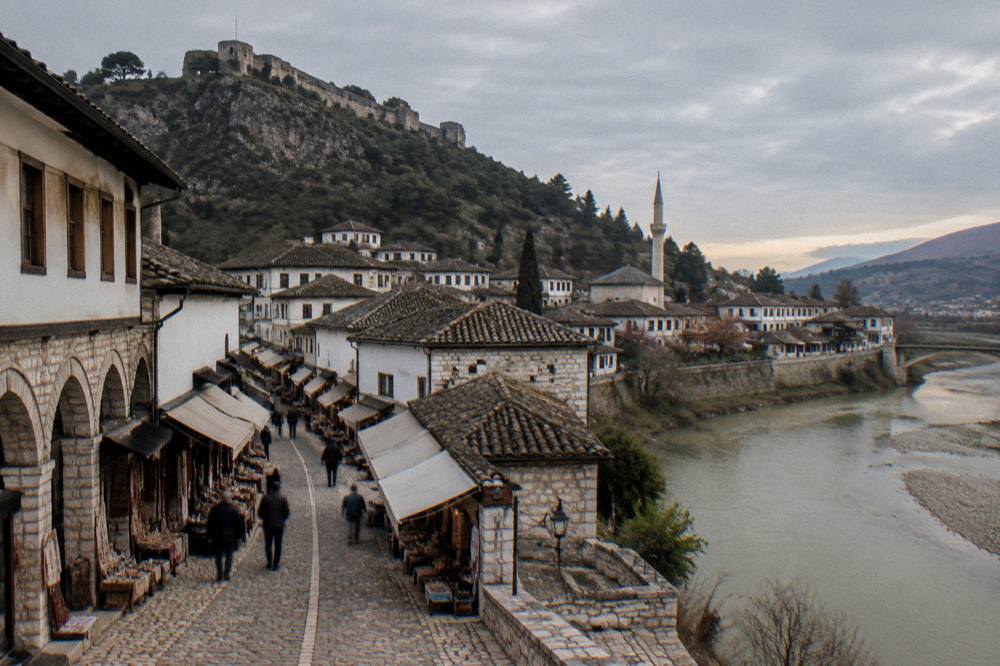 River flowing past stone banks with old houses and a minaret in evening light