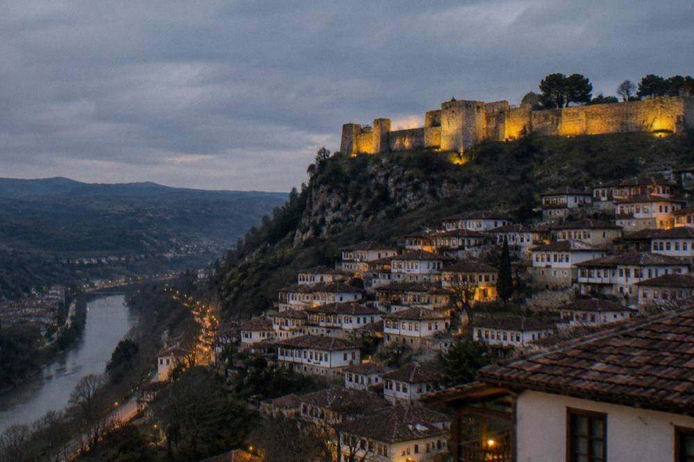 Fortress walls lit at night above a town strung with lights
