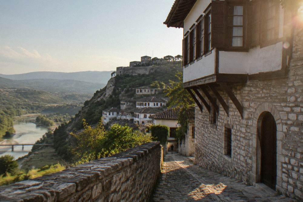 Stone Ottoman-era house with overhanging upper floors and wooden window shutters on a narrow Berat street
