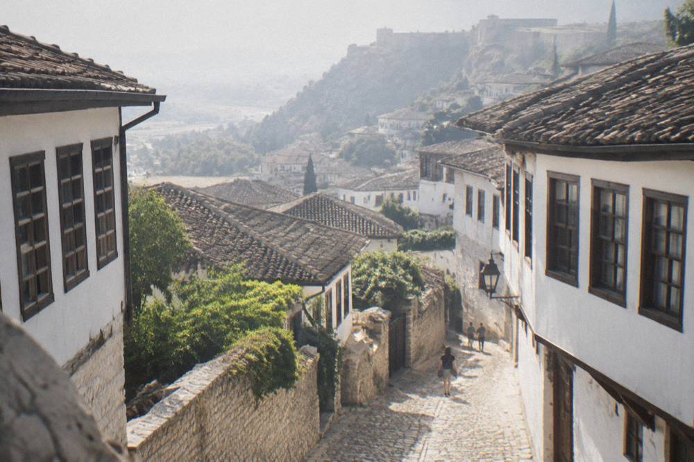 Narrow cobbled lane in Mangalem climbing between white-walled houses with rows of windows