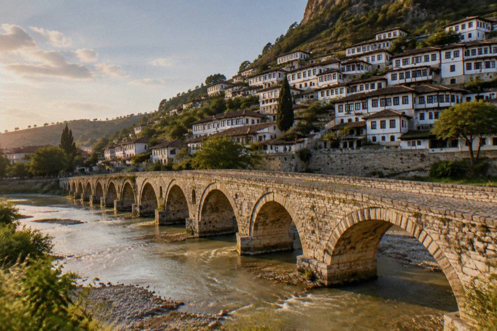 Row of white Ottoman houses with many windows rising up a hillside above a stone bridge at golden hour