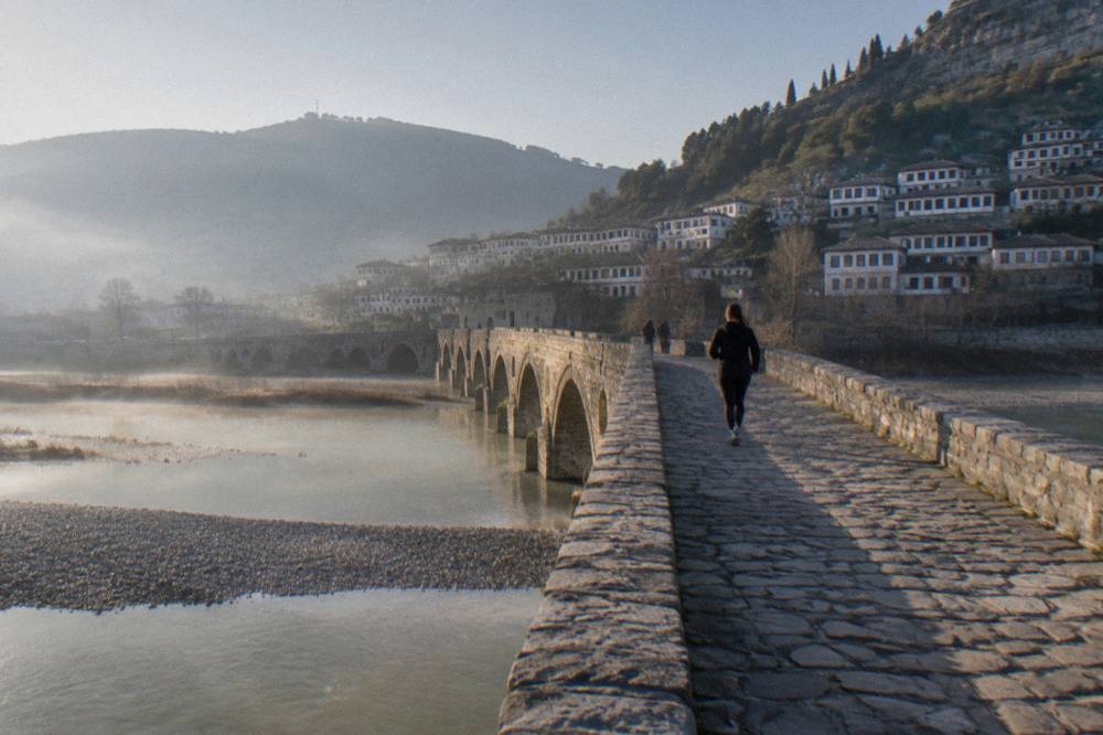 Stone bridge over a river at dawn with mist over the water and hills behind