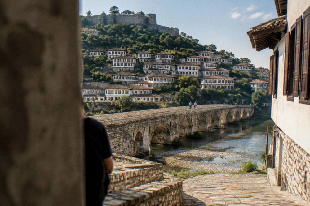 Stone-paved street between whitewashed houses with wooden shutters climbing toward a castle wall