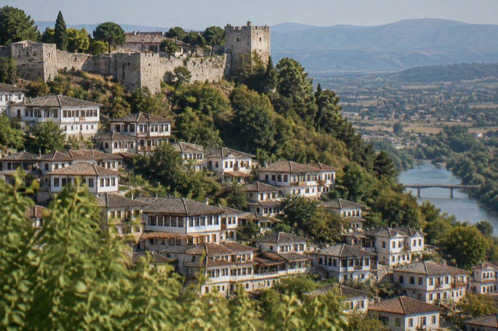 Rows of white Ottoman houses with many windows climbing the hillside beneath Berat Castle