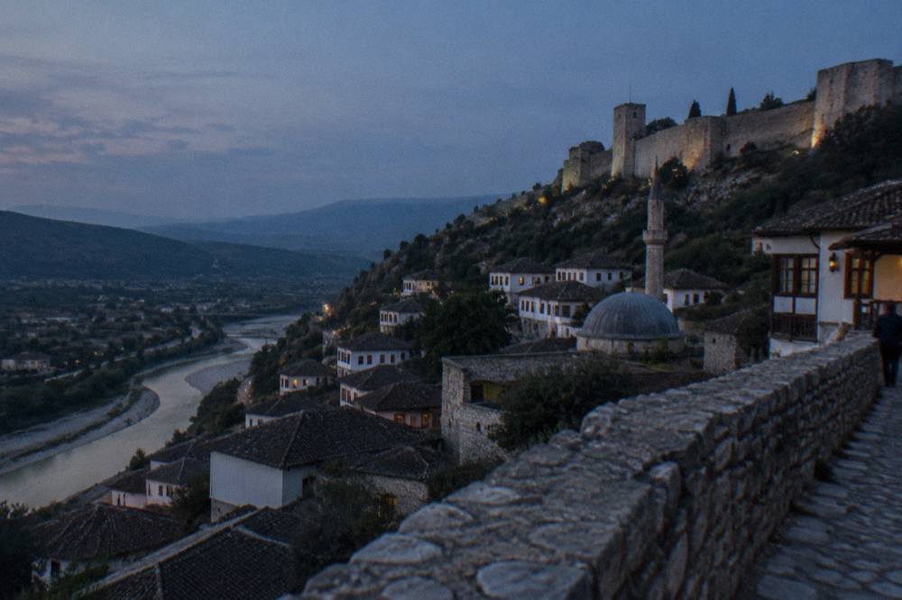 Grey lead dome and stone minaret base of a small mosque seen over rooftops in Berat
