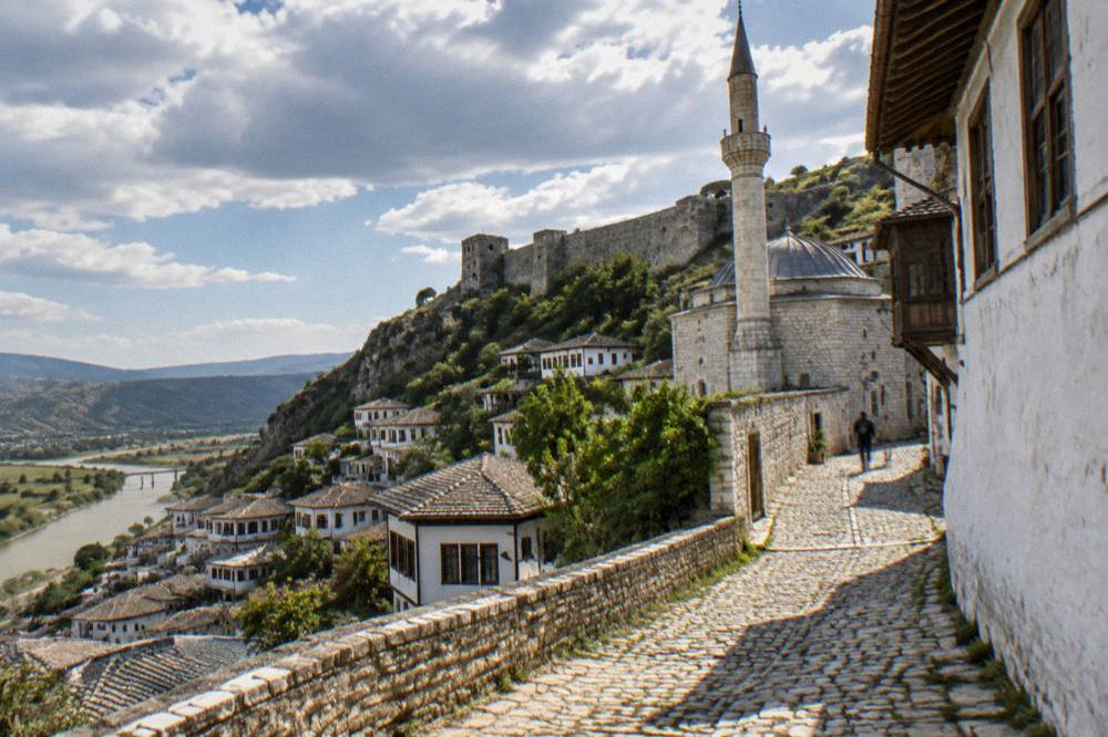 Narrow cobbled lane in Berat climbing between whitewashed houses toward a mosque wall