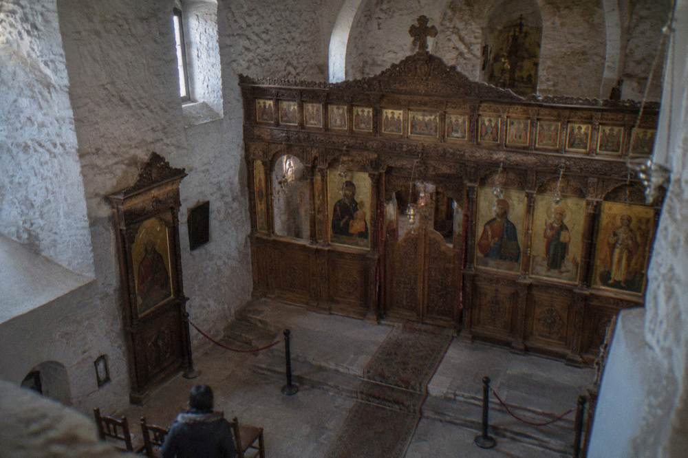 Interior of a stone church with a carved wooden iconostasis and rows of gilded Orthodox icons