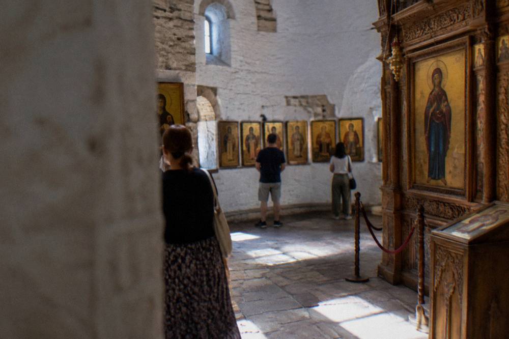 Visitors viewing rows of icons along the stone walls of a church museum gallery