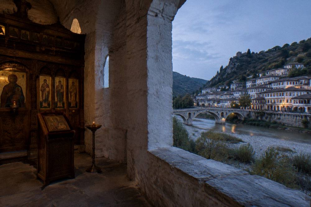 Panorama of whitewashed houses with rows of windows overlooking a river and an old stone bridge