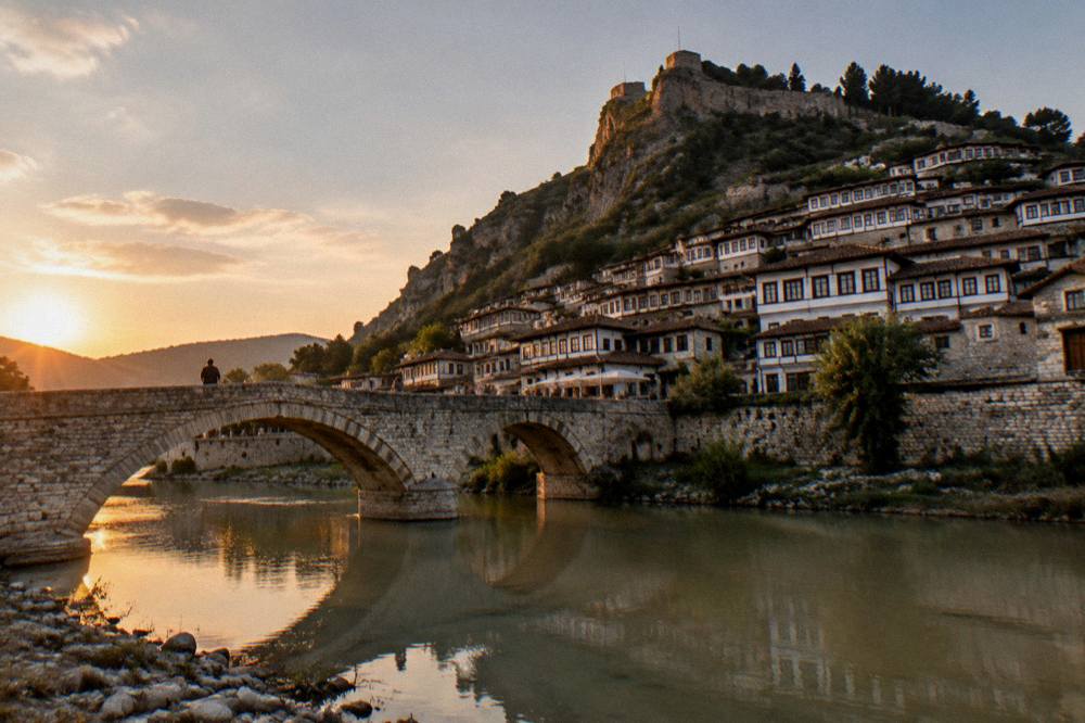 Old stone bridge over a calm river at dusk with Ottoman houses reflected in the water
