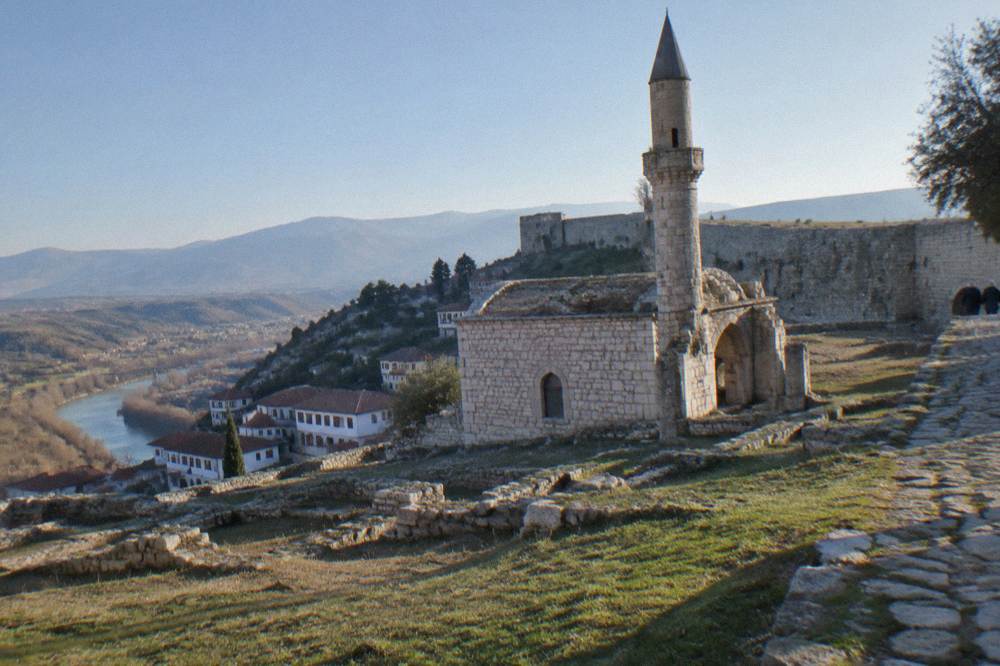 Stone ruins of a small mosque with a round minaret inside the walls of Berat Castle under a clear sky