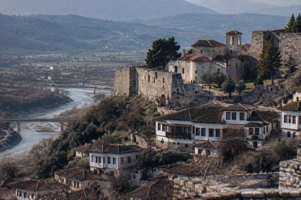 A stone Orthodox church with a tiled roof and a small bell tower above the white Ottoman houses of Berat