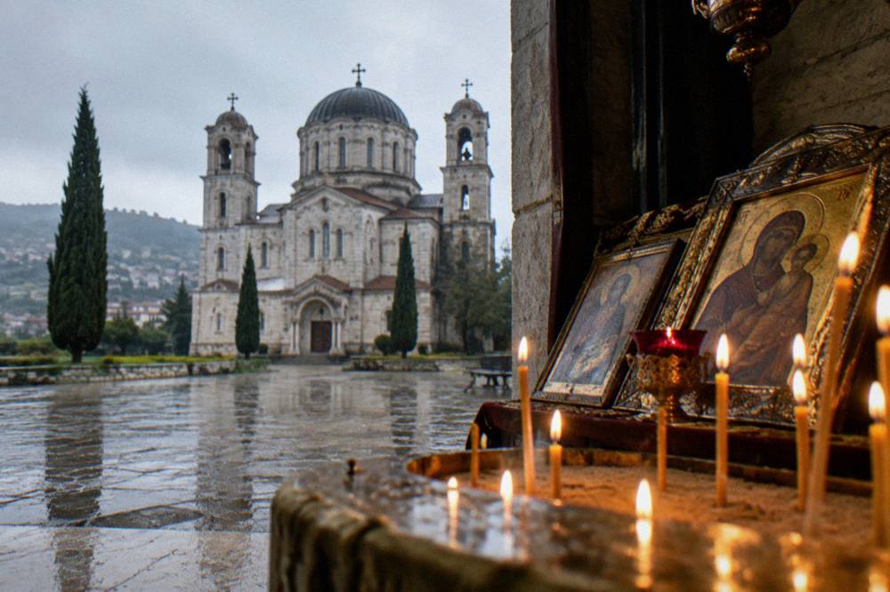 The interior of a small Orthodox church with rows of candles and gilded icons on an icon stand