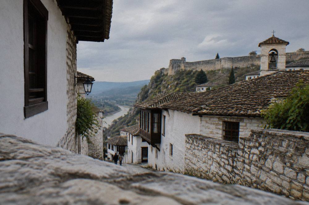 Narrow stone lane in Berat with whitewashed Ottoman houses and a small bell tower above the rooftops