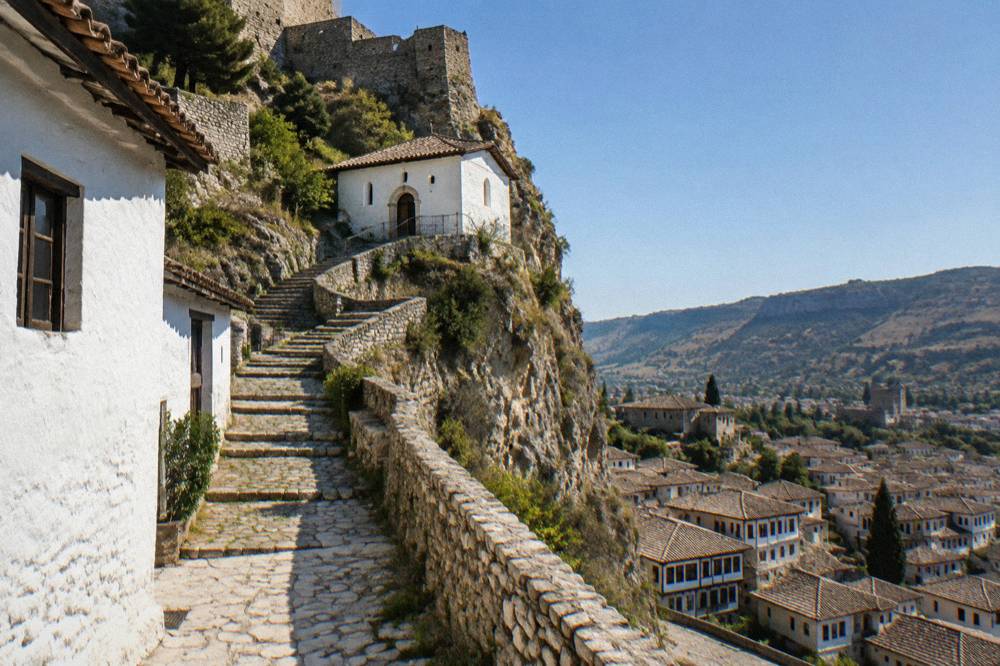 Stepped stone lane climbing between whitewashed houses toward the castle walls of Berat