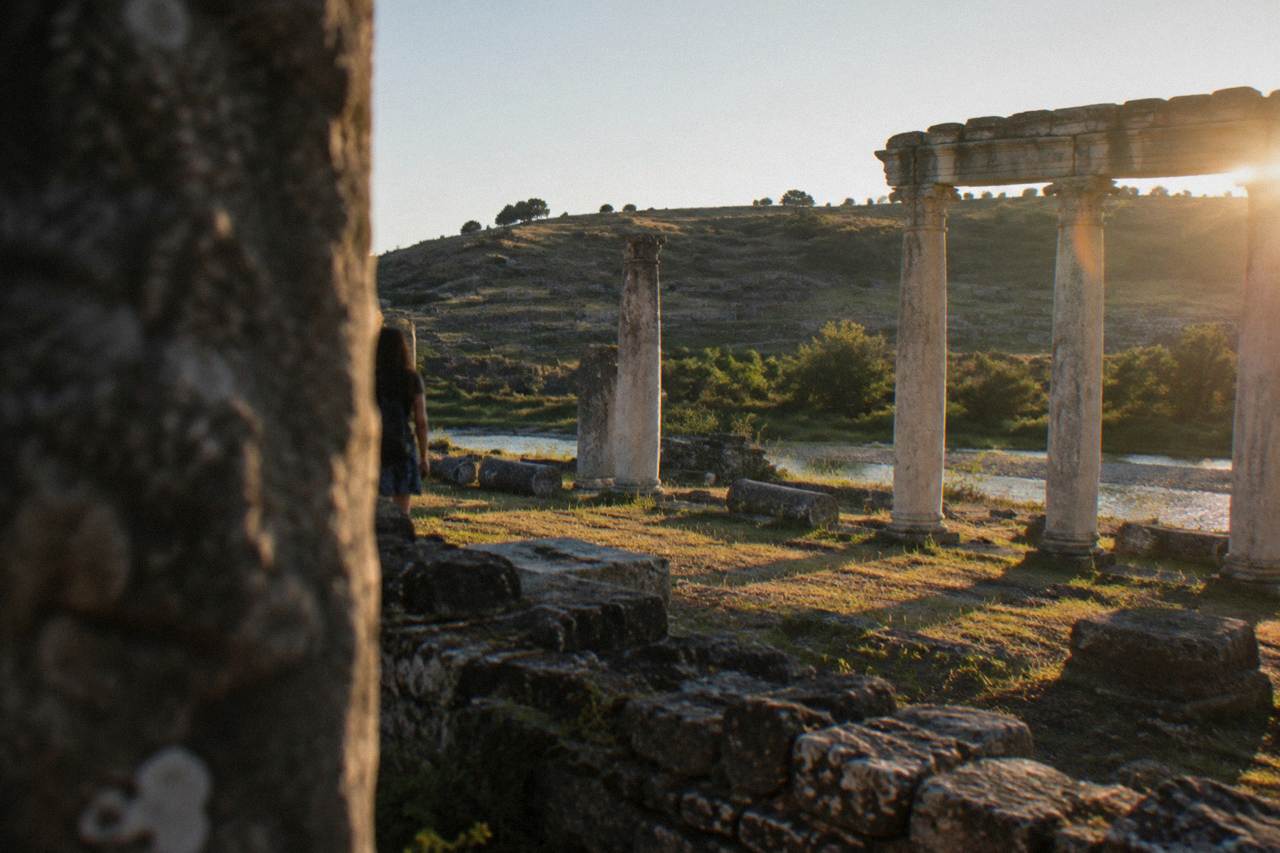 Ancient stone columns and hillside ruins of an archaeological site under a clear sky