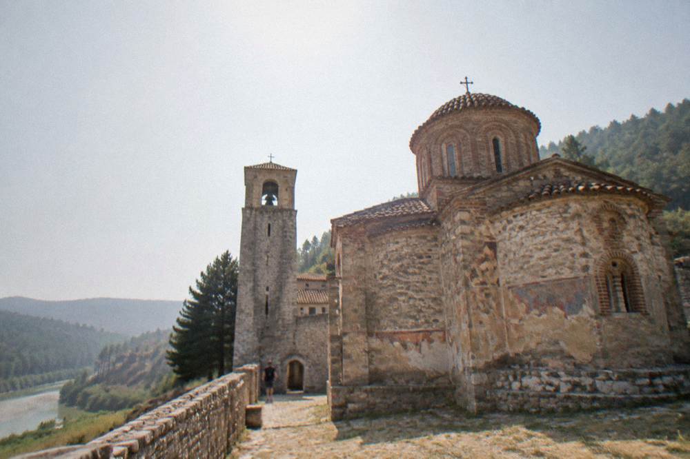 A hilltop monastery with a bell tower and walled courtyard overlooking pine-covered hills