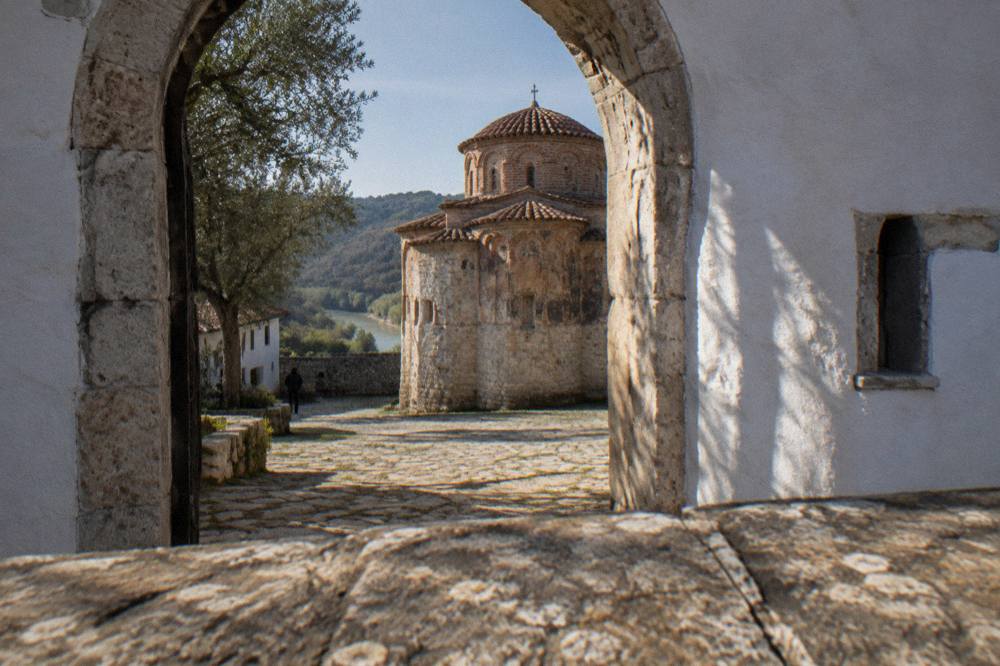 White monastery walls and a small domed church seen through an arched gate